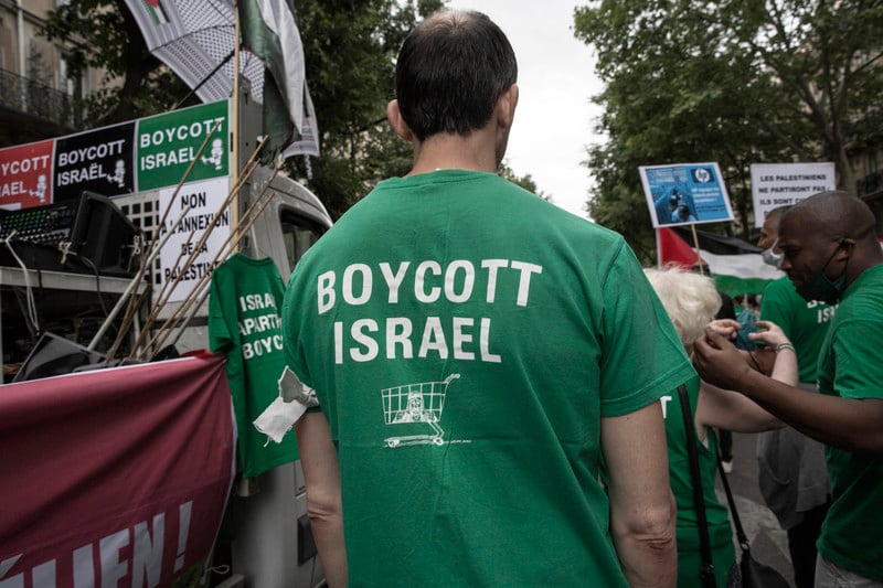 Man in crowd wears T-shirt reading Boycott Israel with icon of a shopping cart