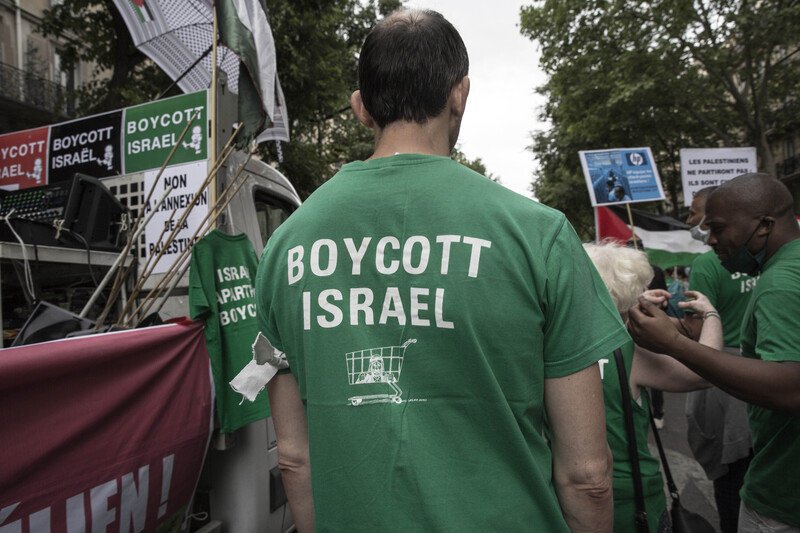 Man in crowd wears T-shirt reading Boycott Israel with icon of a shopping cart