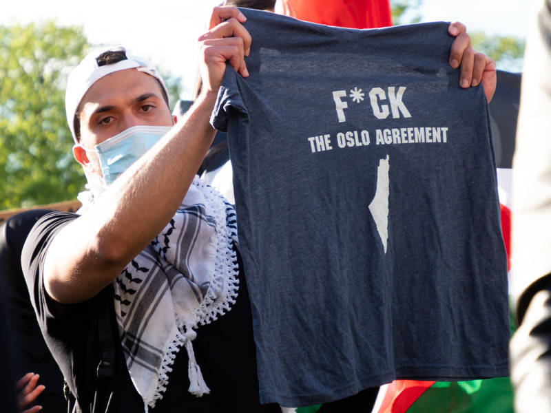 Man wearing kuffiyeh around his neck holds up T-shirt reading F*CK the Oslo agreement