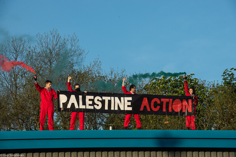 Four red-suited people hold a banner reading "Palestine Action"