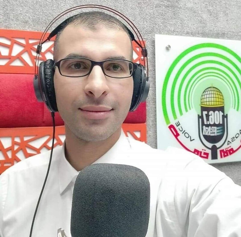 Man seen from chest up wears headphones while sitting in front of microphone in sound booth