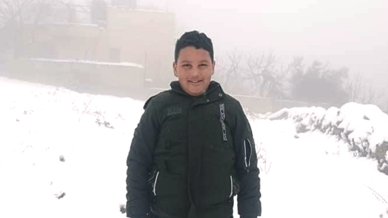 A boy wearing a coat stands in the snow 