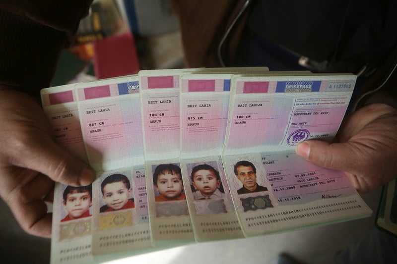 A pair of hands holds five passports opened to page showing photos