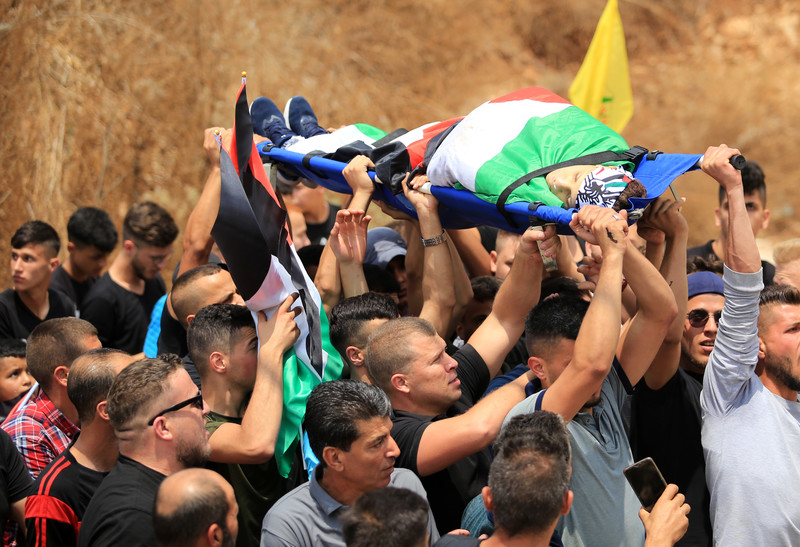 Men carry the body of a boy wrapped in a flag on a stretcher 