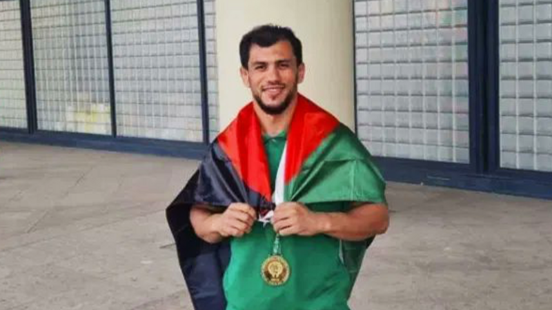 The Palestinian flag is draped around the shoulders of a smiling man 