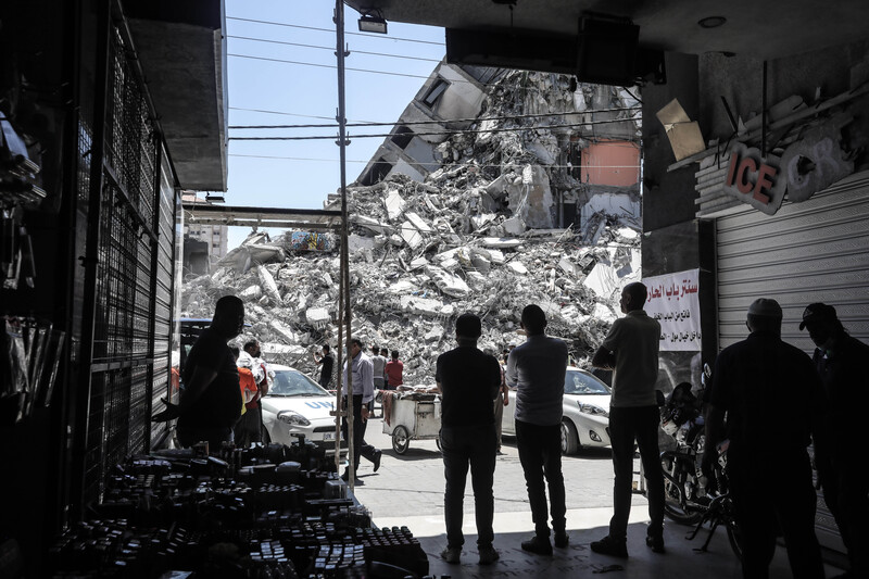 Silhouetted people stand in front of giant mound of rubble from a destroyed building