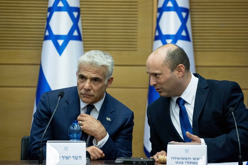 Two seated men with Israeli flags behind them confer