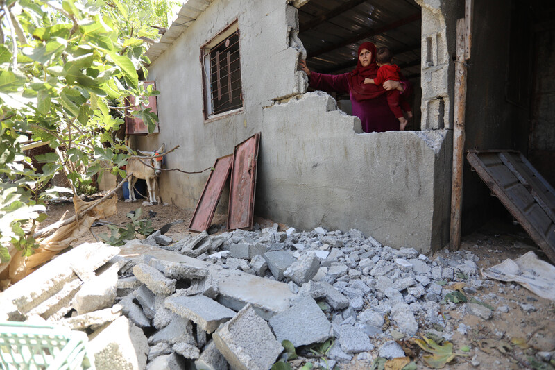 A woman stands behind the remains of a wall of her home