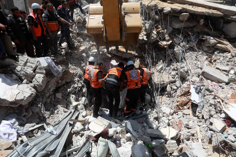 Men in florescent vests stand next to excavator machine atop rubble