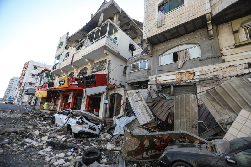 Cars on commercial street are crushed by debris from nearby bombed buildings