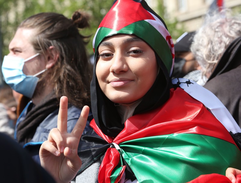 A woman draped in the Palestinian flags flashes the victory sign