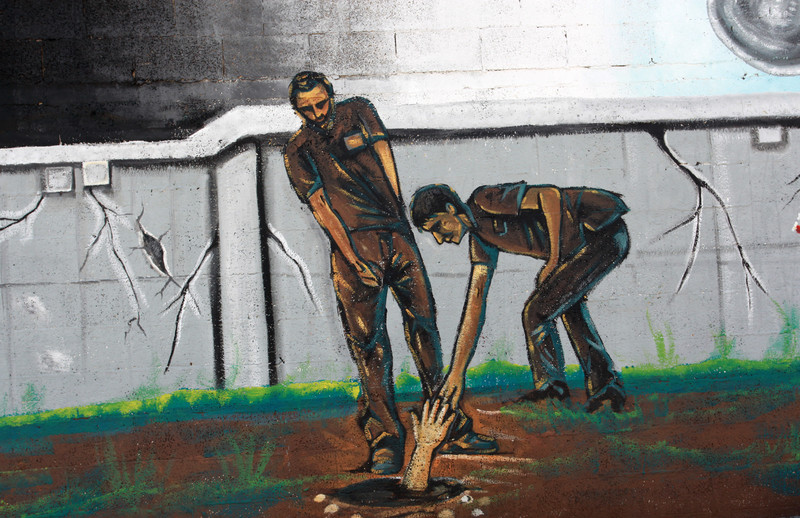 A mural depicts two men reaching out for a hand in a hole in the ground 