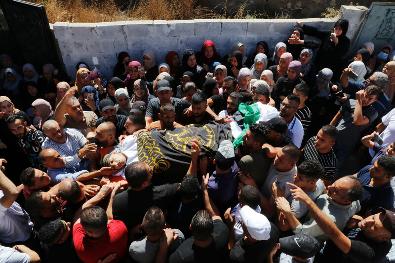 Crowds carry a body wrapped in a shroud and flags 