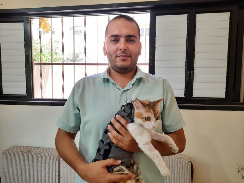 A man holds a cat wearing a black vest
