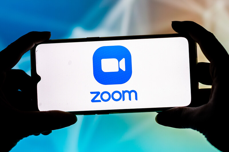 Fingers hold a smartphone displaying Zoom logo