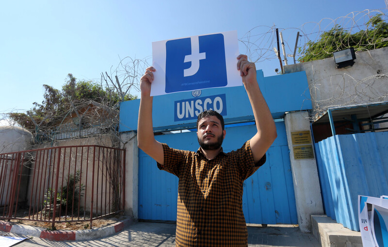 A man holds the Facebook logo upside down in front of the UNSCO building