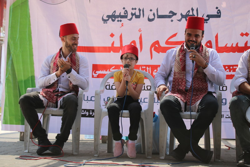 A young girl speaks into a microphone flanked by two men