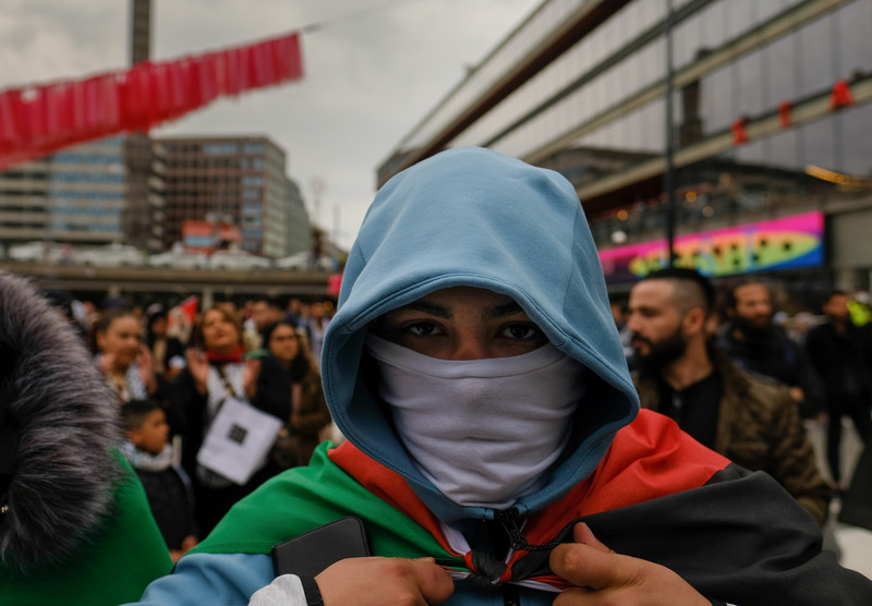 Close up of man in face mask and hoodie carrying Palestinian flag