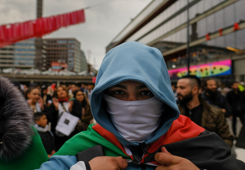 Close up of man in face mask and hoodie carrying Palestinian flag