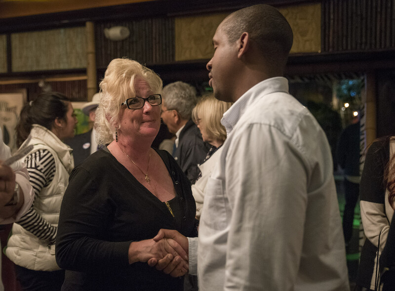 A man and a woman shake hands with people in background