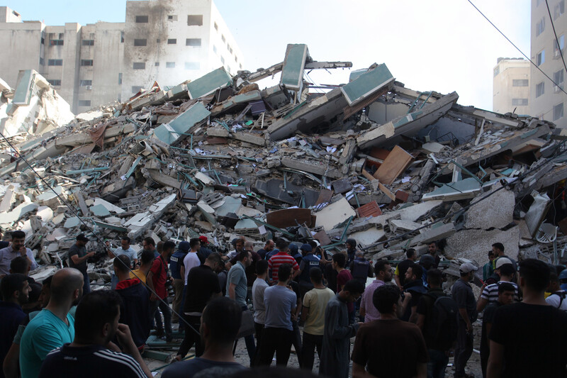 Crowd stands in front of a mound of rubble