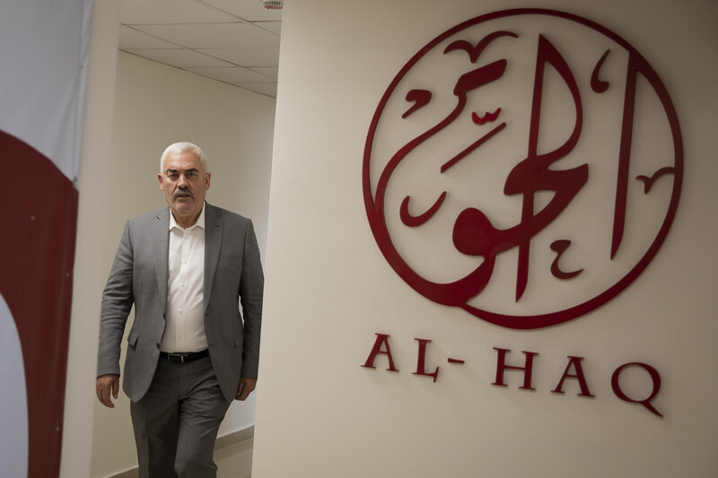 Man stands next to Al-Haq logo on wall