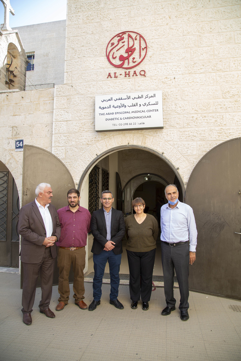 Five people stand outside of a building with Al-Haq's logo on the facade