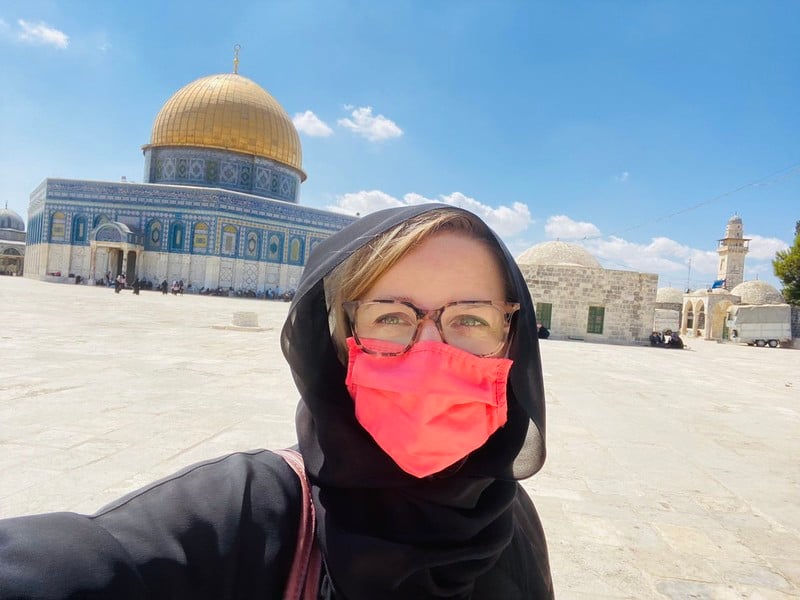 Woman in face mask stands in front of Jerusalem's Dome of the Rock