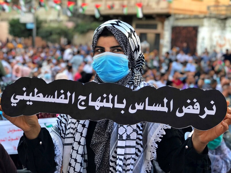 A woman in a face mask holds up a banner in Arabic