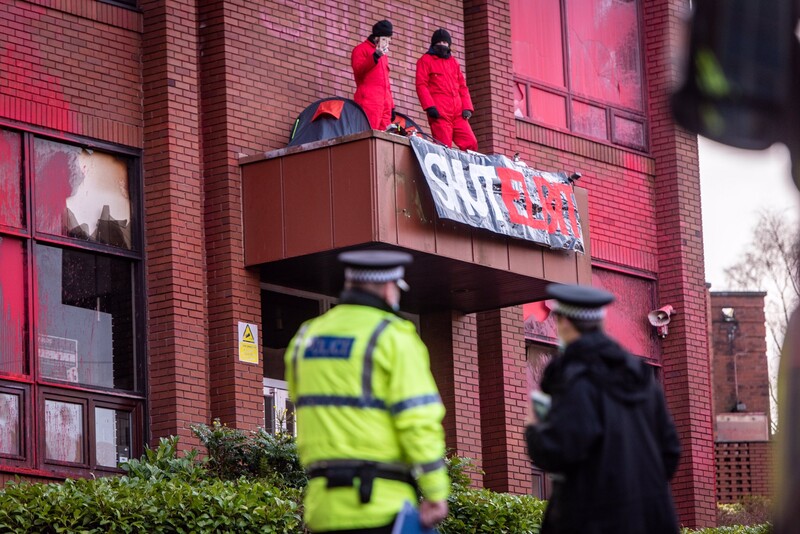 Police watch two activists occupy a rooftop