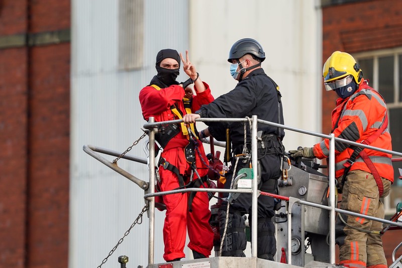 A man in handcuffs being removed by fire fighters gives the victory sign