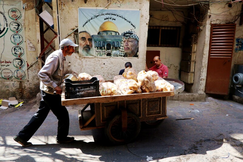 A man pushes a cart with bread in front of a poster depicting the al-Aqsa mosque in Jerusalem