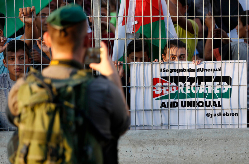 A soldier takes a picture of protestors safely behind a metal cage