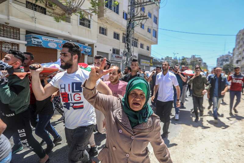 A older woman makes a victory sign with her hand while walking in funeral procession