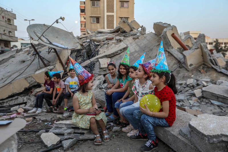 Children wearing birthday hats sit on rubble