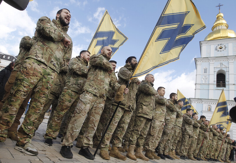 Men in military uniforms parade holding banners