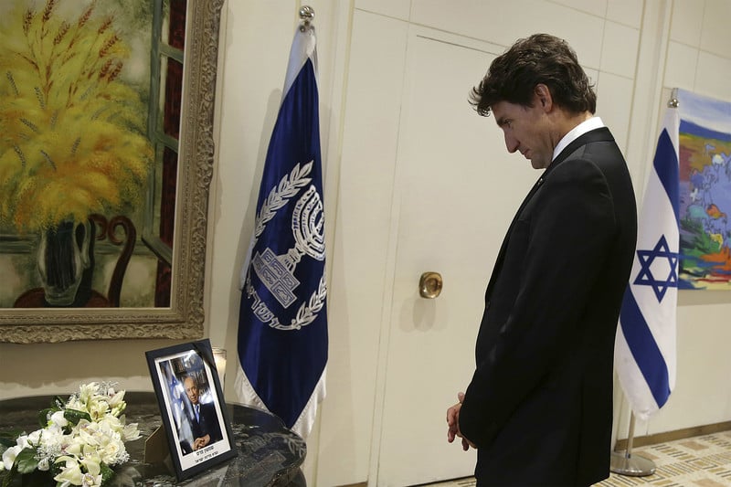 Justin Trudeau looks at a photograph of Shimon Peres next to a bouquet