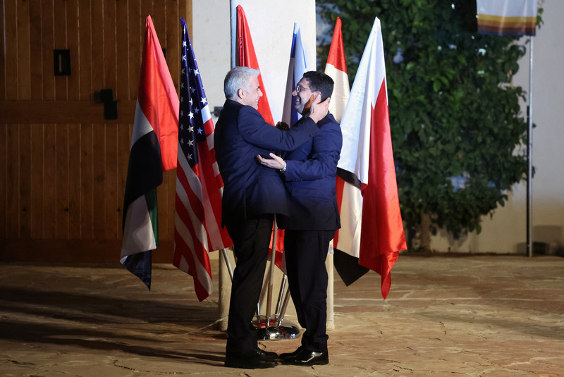 Two men in suits embrace in front of several flags 