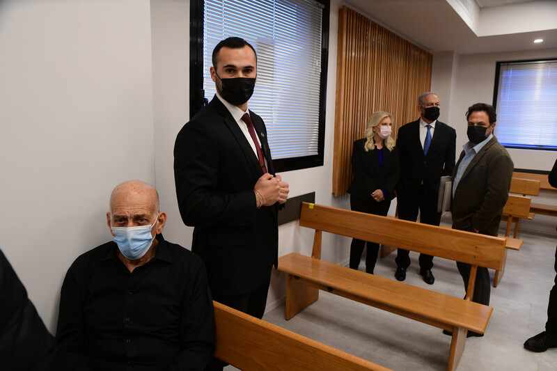 Ehud Olmert in court foreground with Netanyahus in background