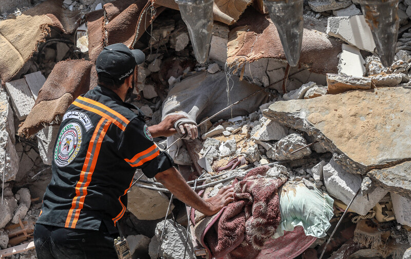 Civil defense worker touches arm protruding from under rubble