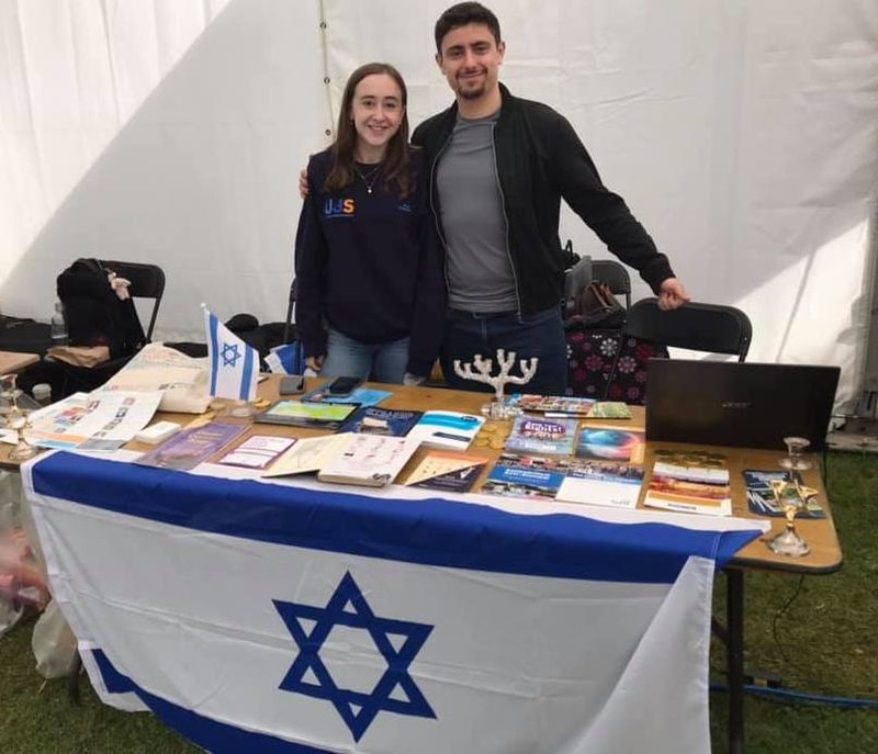 A woman and a man at a stall draped in an Israeli flag