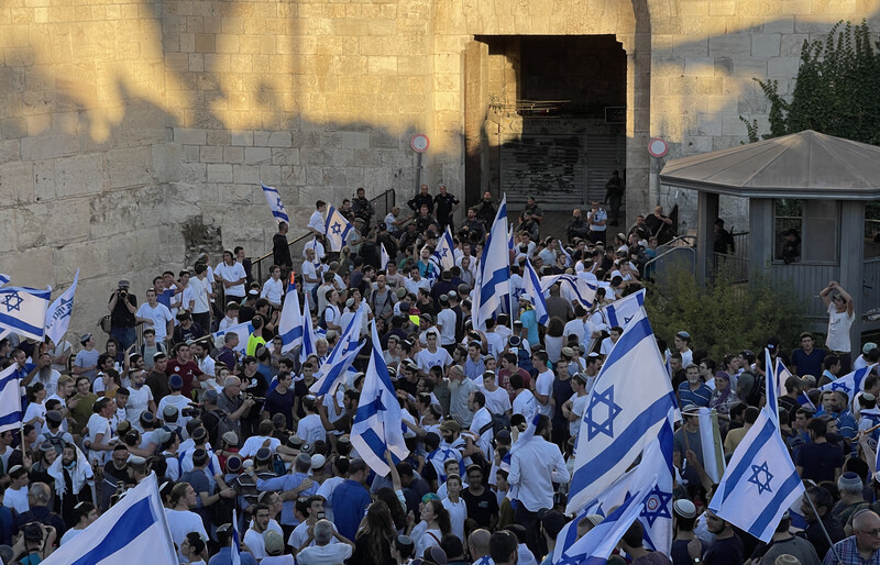 Large group of people with flags against backdrop of ancient stone wall