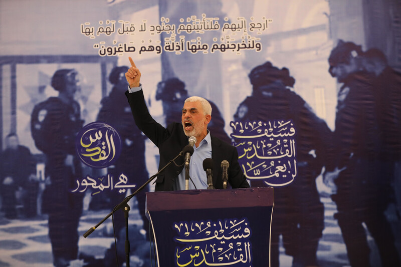 Man in a suit gives a speech at a podium against a backdrop 