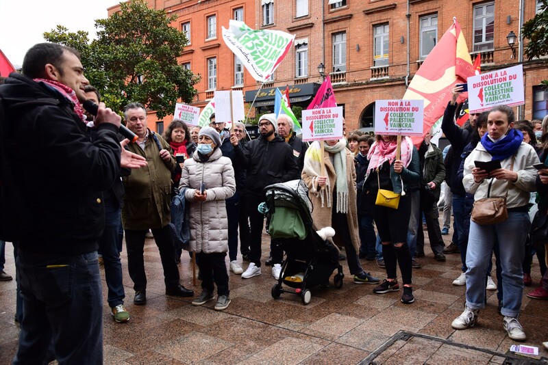A man with a microphone addresses people holding signs in a street