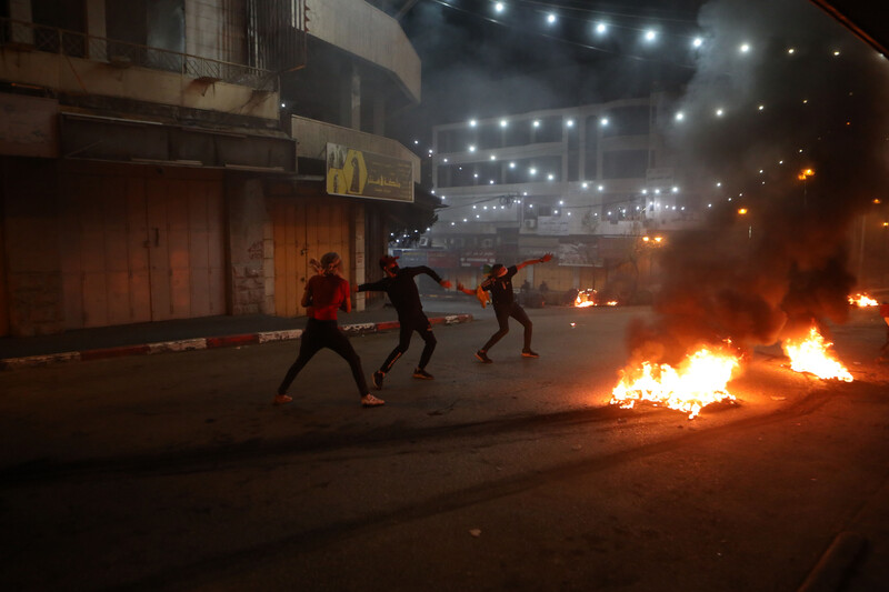 Three masked men wield slingshots next to a fire