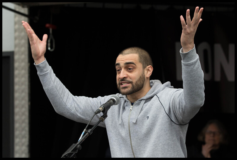 A man raises his arms while speaking into a microphone