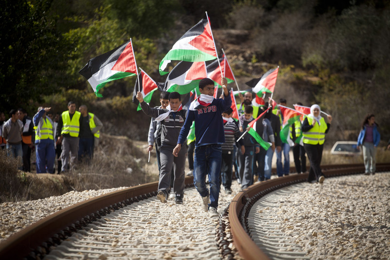 A group of people carrying flags walks along track as others watch