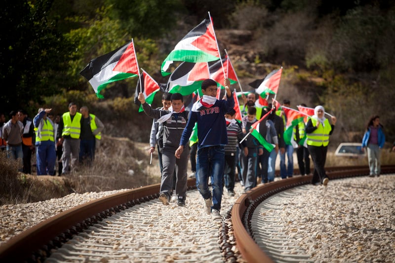 A group of people carrying flags walks along track as others watch