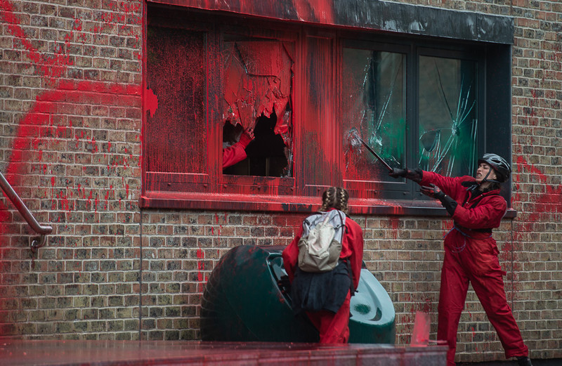 A woman smashes windows of an office building daubed with red paint