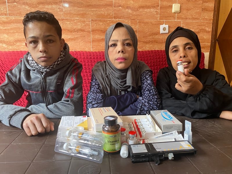 Three people sit at a table laden with medicines